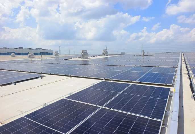 Rooftop of a building covered with multiple rows of dark blue solar panels under a bright sky with clouds.