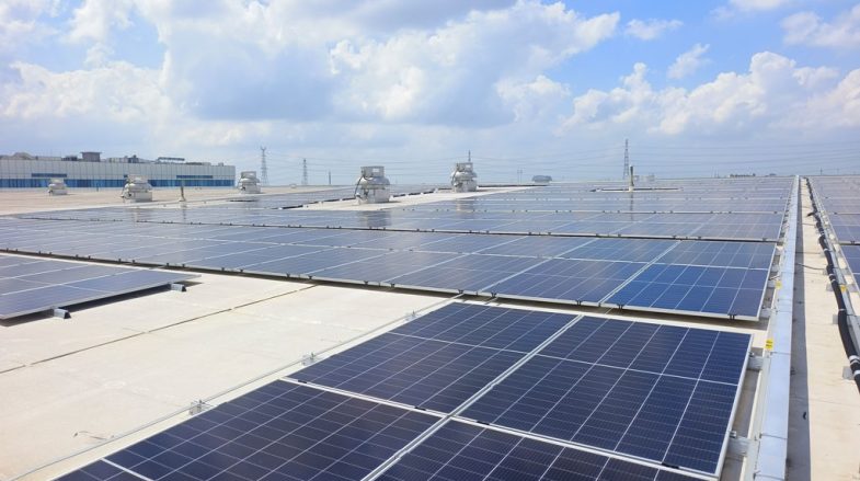 Rooftop of a building covered with multiple rows of dark blue solar panels under a bright sky with clouds.